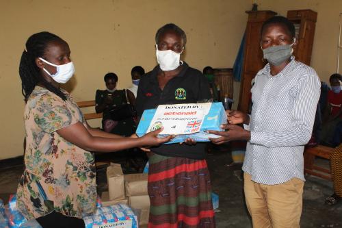 FVA Projects Officer (left) and Executive Secretary of Gishyike Cell, Rwabicuma Sector, Nyanza LRP (right) handing a box of soap over to a women’s saving group representative (center) who will later distribute 3 bars of soap to each group member. 